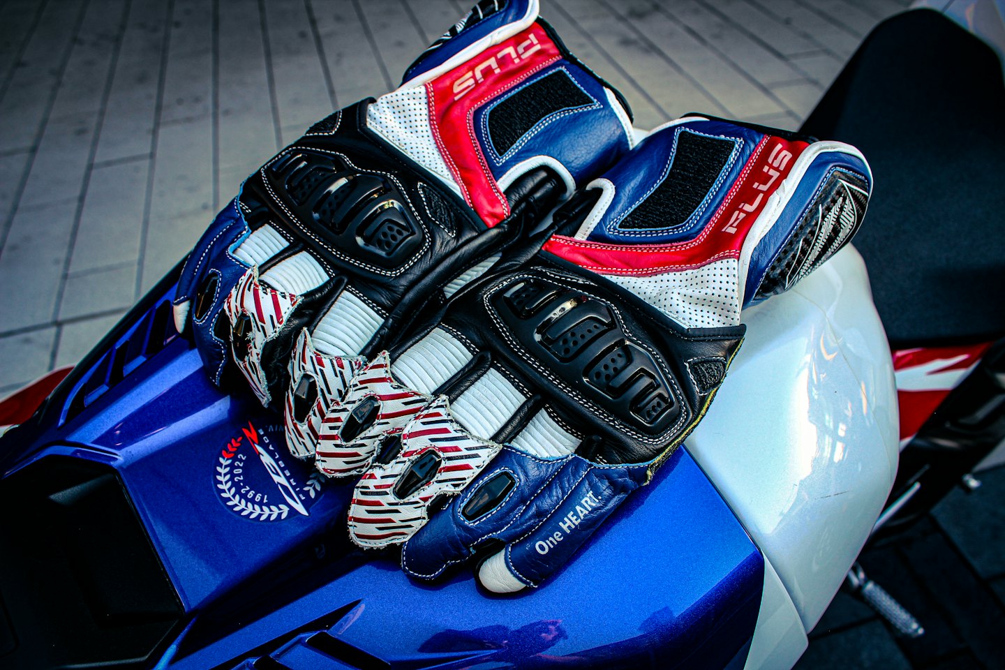Guanti da moto da corsa appoggiati su una moto blu e bianca.