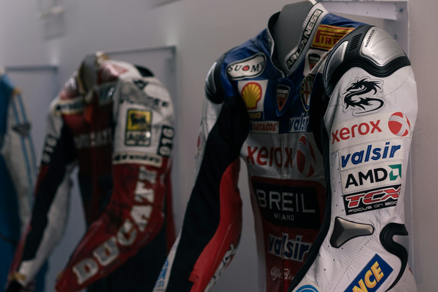 Tute da moto da competizione esposte su manichini in una sala espositiva.